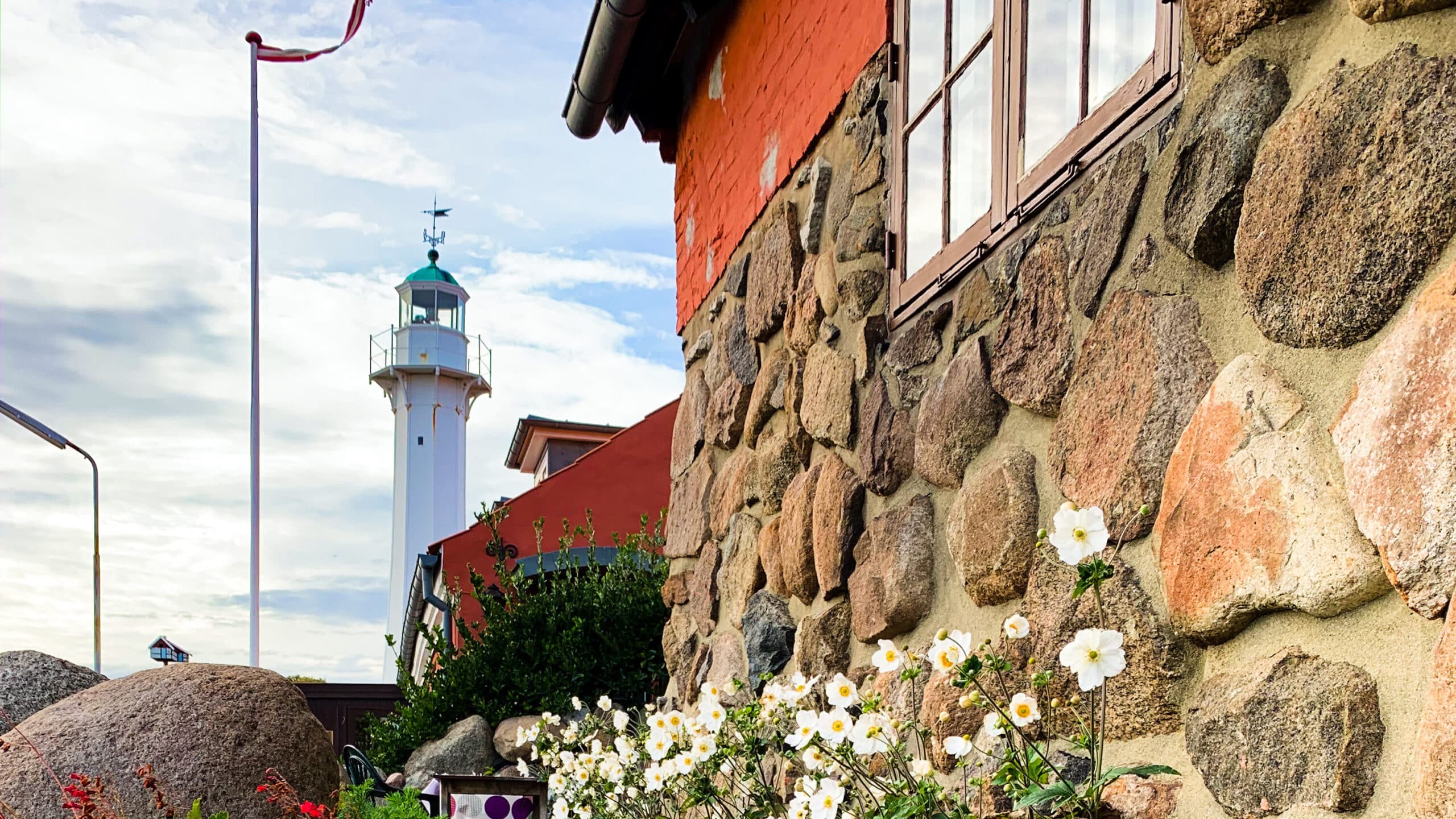 Weißer Leuchtturm Rønne Bagfyr hinter einer Steinmauer mit Blumen