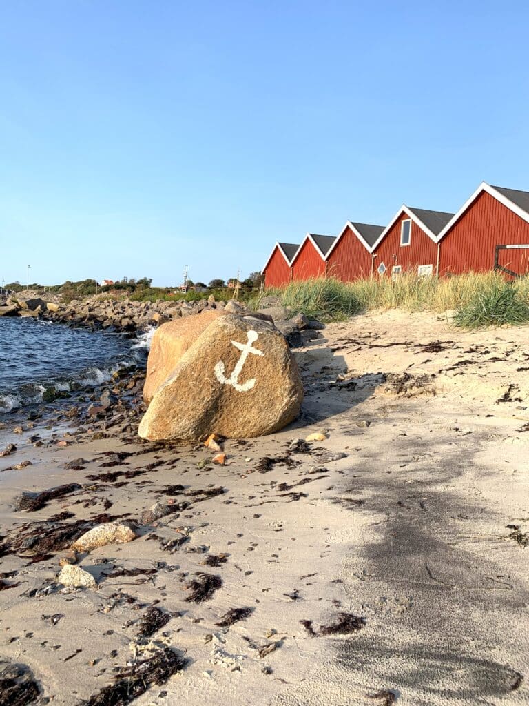 Findling mit aufgemaltem Anker am Strand und rote Häuschen in Hasle