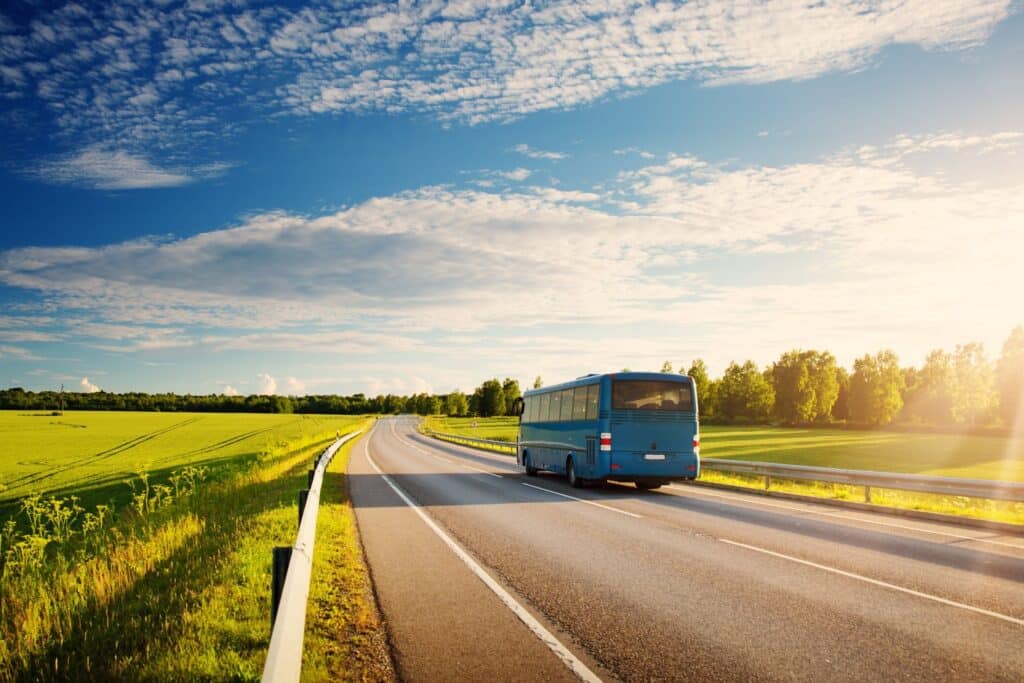 Blauer Reisebus auf einer leeren Landstraße zwischen grünen Feldern an einem sonnigen Tag