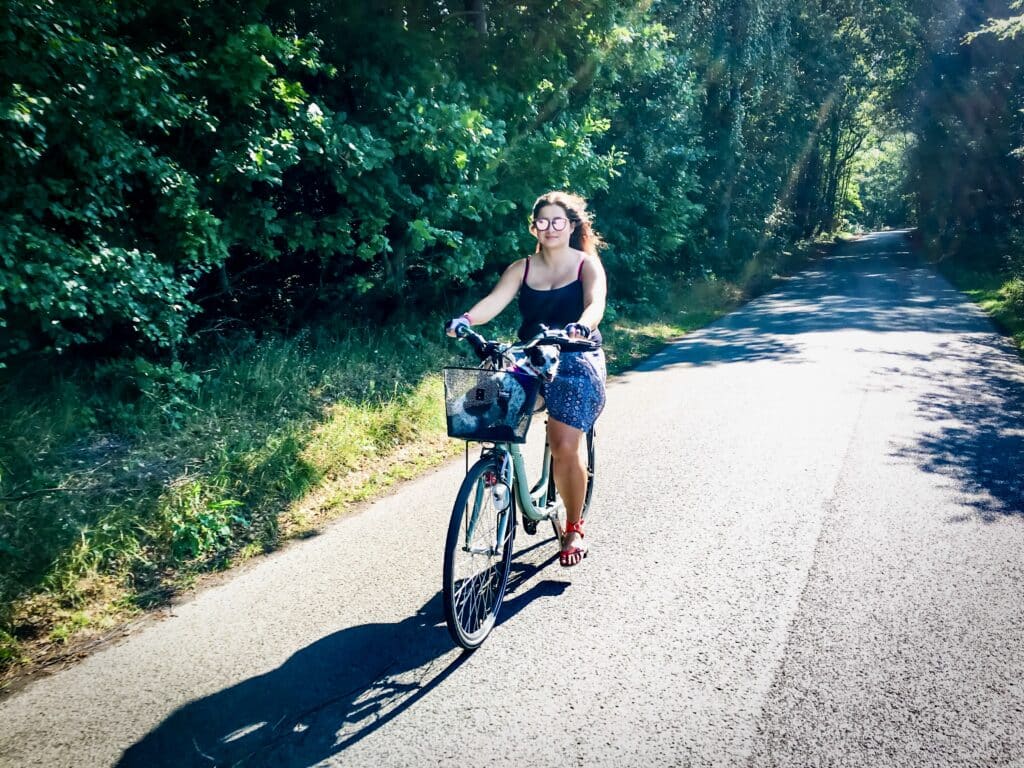 Frau fährt mit Fahrradkorb über einen Waldweg an einem sonnigen Tag