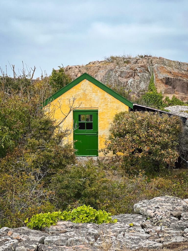 Kleines gelbes Haus mit grüner Tür zwischen Felsen und Sträuchern