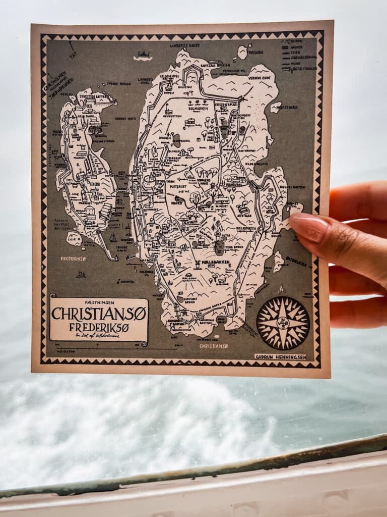 Hand mit einer illustrierten Karte von Christiansø und Frederiksø vor dem Meer