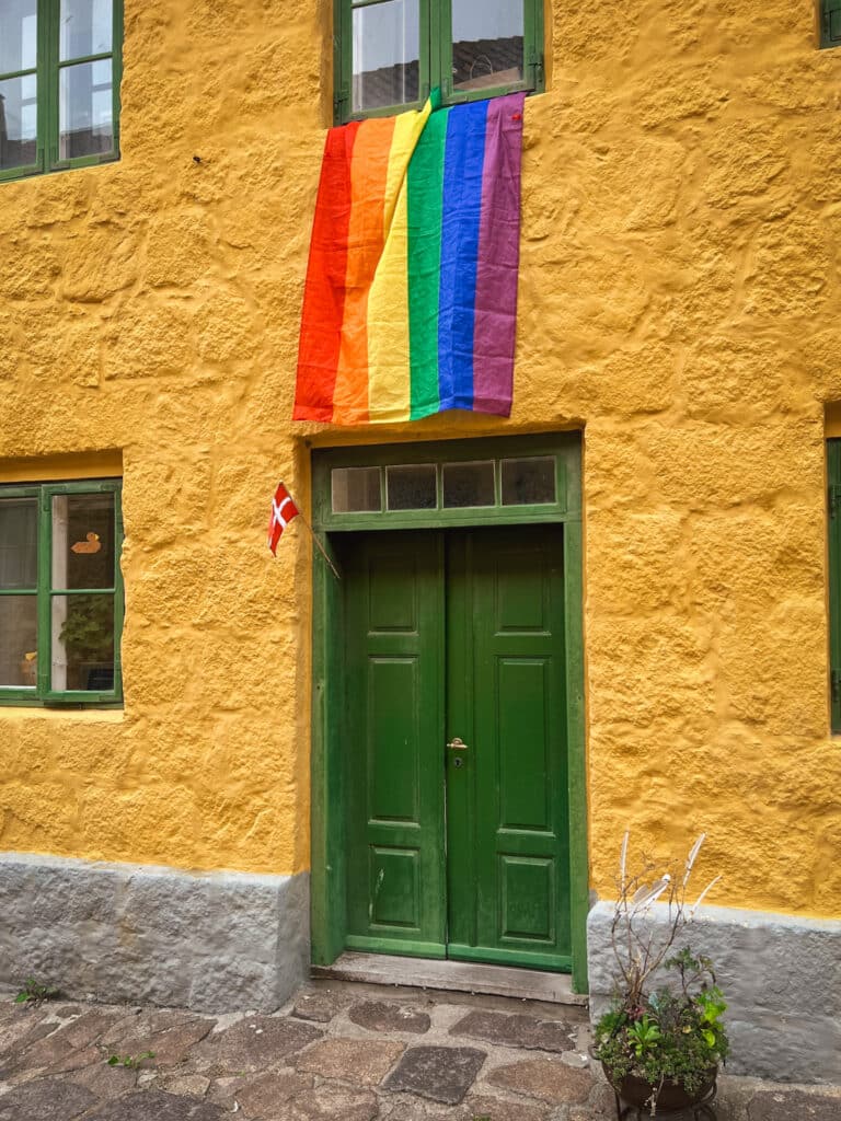 Grüne Tür in einer gelben Wand, darüber eine Regenbogenfahne