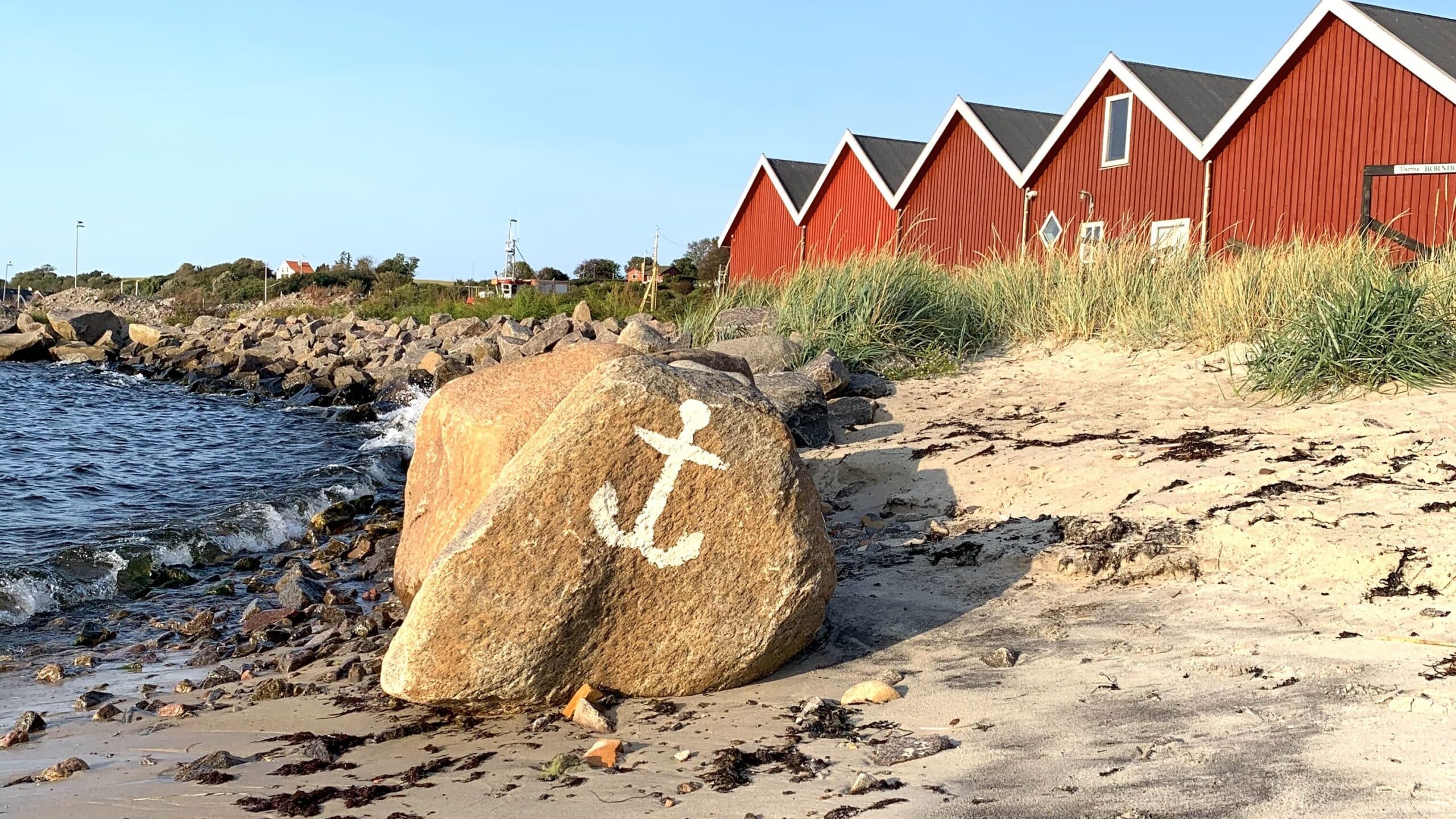 Findling mit aufgemaltem Anker und rote Hütten am Strand von Hasle