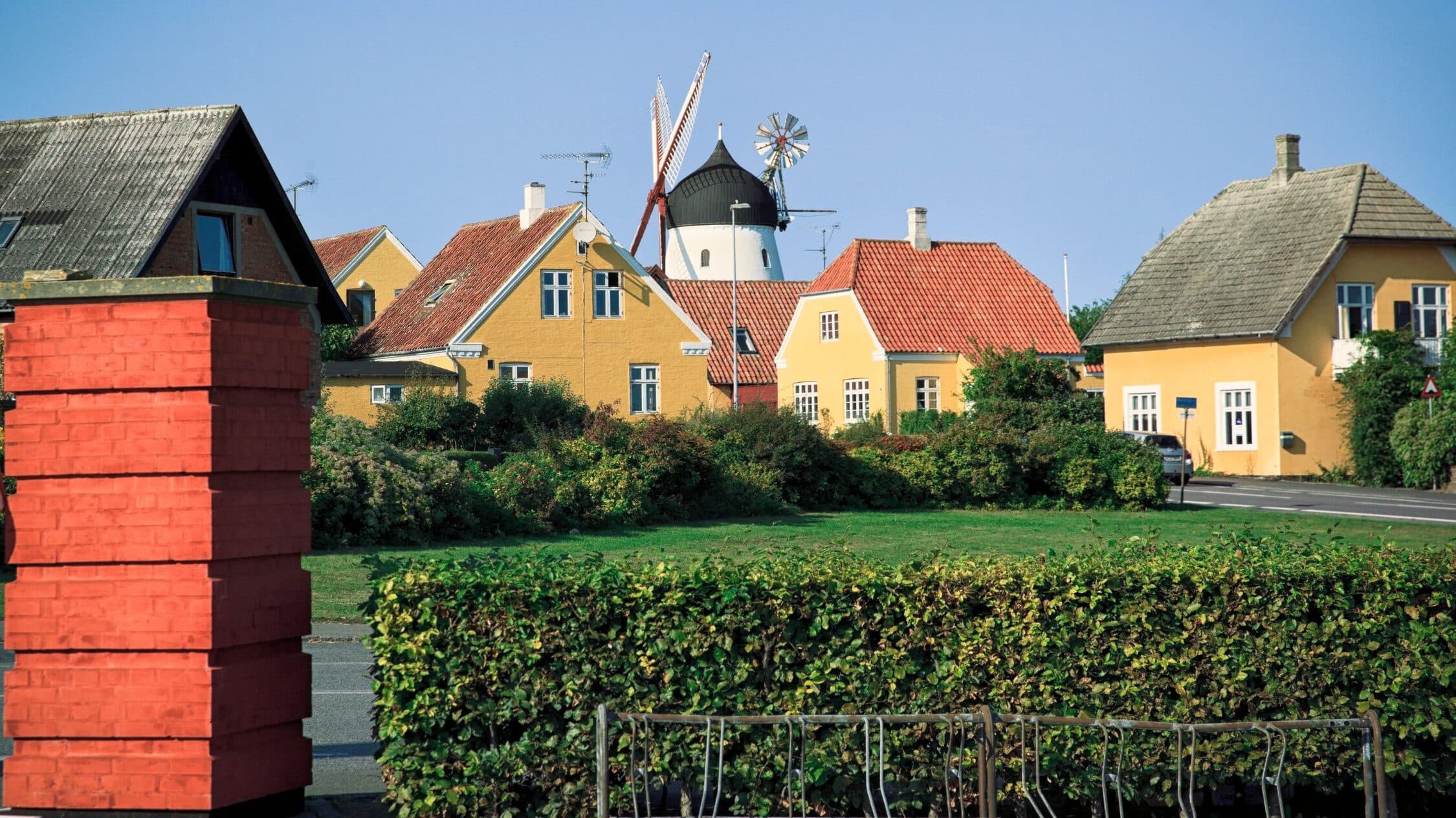 Gelbe Häuser mit roten Dächern und eine Windmühle hinter einer Hecke