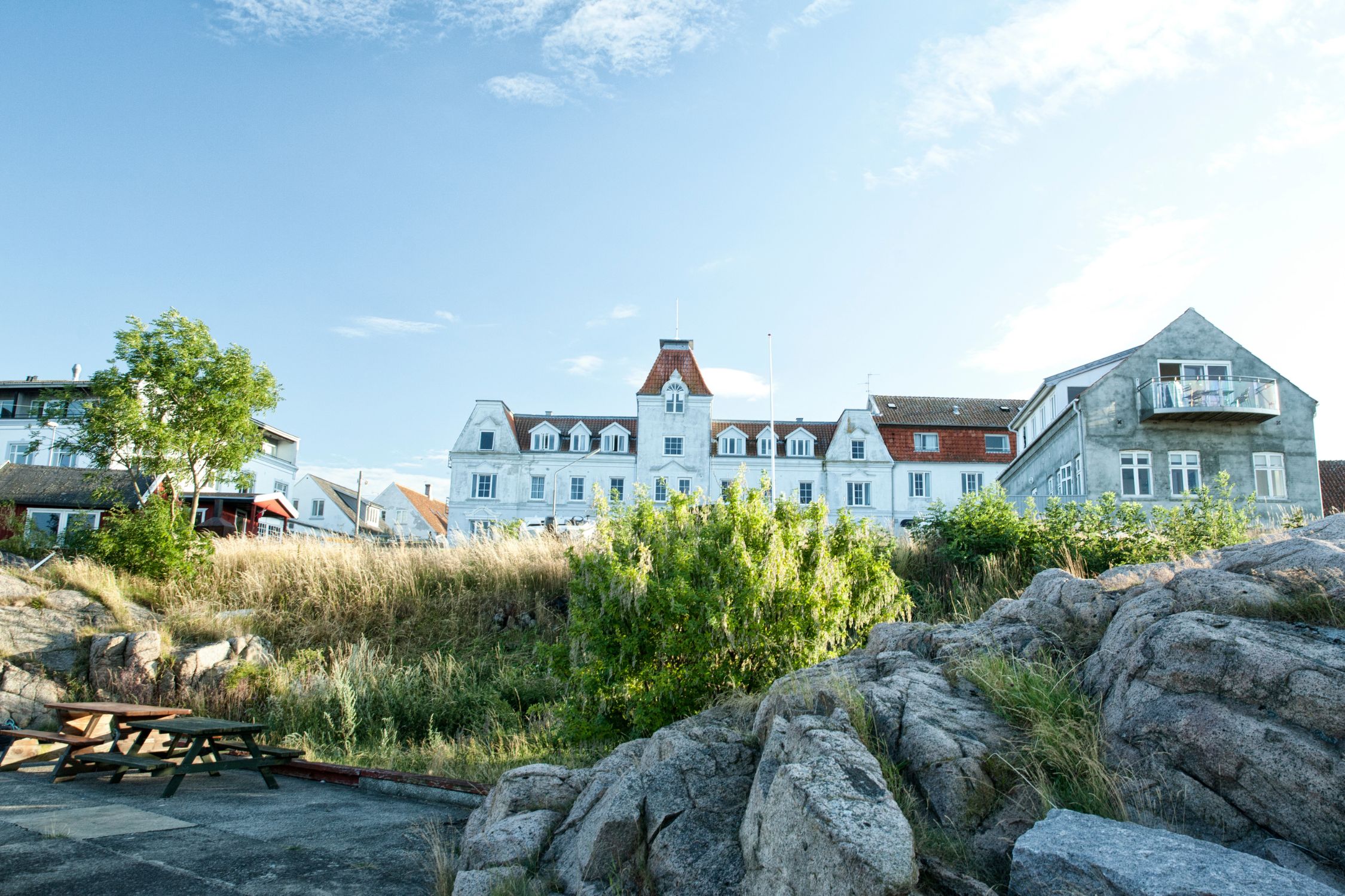 Großes weißes Gebäude mit Türmchen und Gauben über Granitfelsen, im Vordergrund ein Picknicktisch