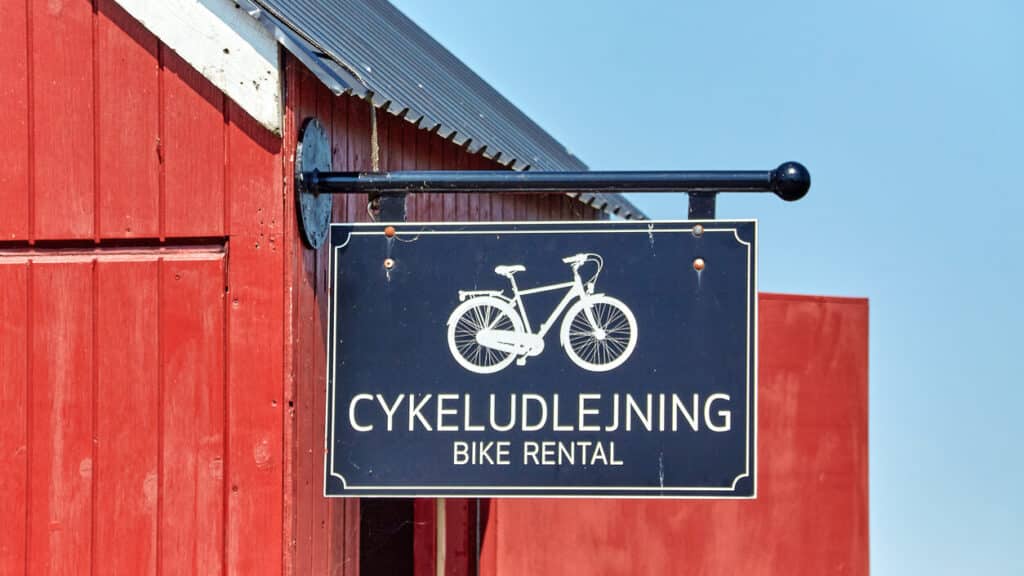 Schild eines Fahrradverleihs (dän. Cykeludlejning) an einem roten Holzhaus