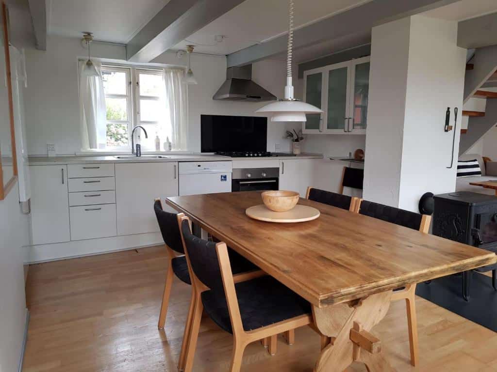 Helle Küche mit Holztisch und Stühlen, dahinter eine Treppe ins Obergeschoss