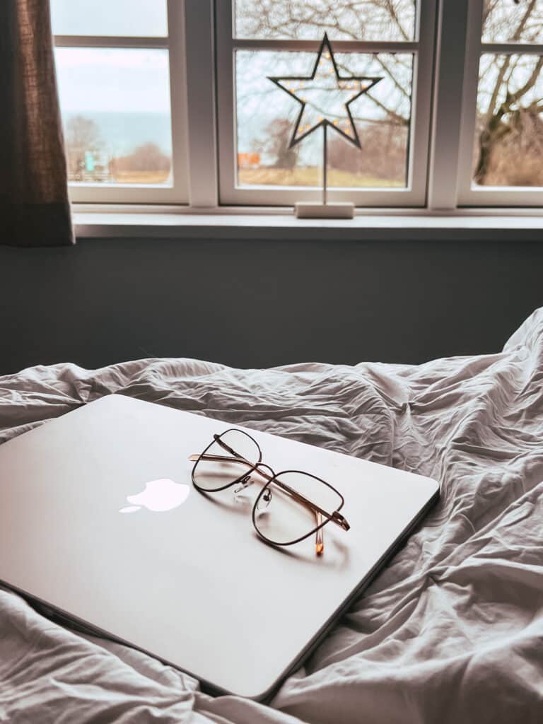 Laptop und Brille auf der Bettdecke, im Fenster ein leuchtender Stern, dahinter das Meer