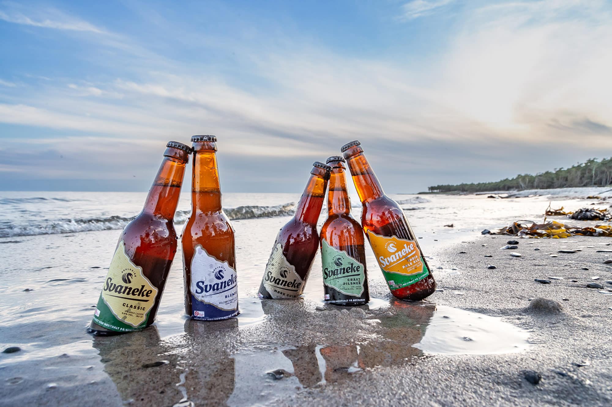 Fünf Flaschen Svaneke-Bier im nassen Sand am Strand