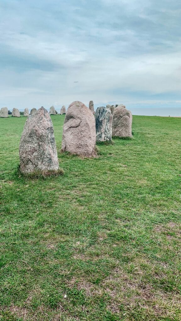 Reihe der Steine von Ales Stenar auf grünem Gras unter bewölktem Himmel