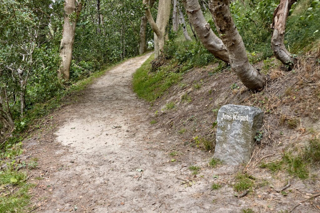 Waldweg und ein Stein mit der Aufschrift Jons Kapel