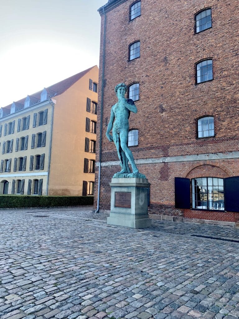 Bronzekopie des David vor einem Backsteinspeicher auf einem gepflasterten Platz
