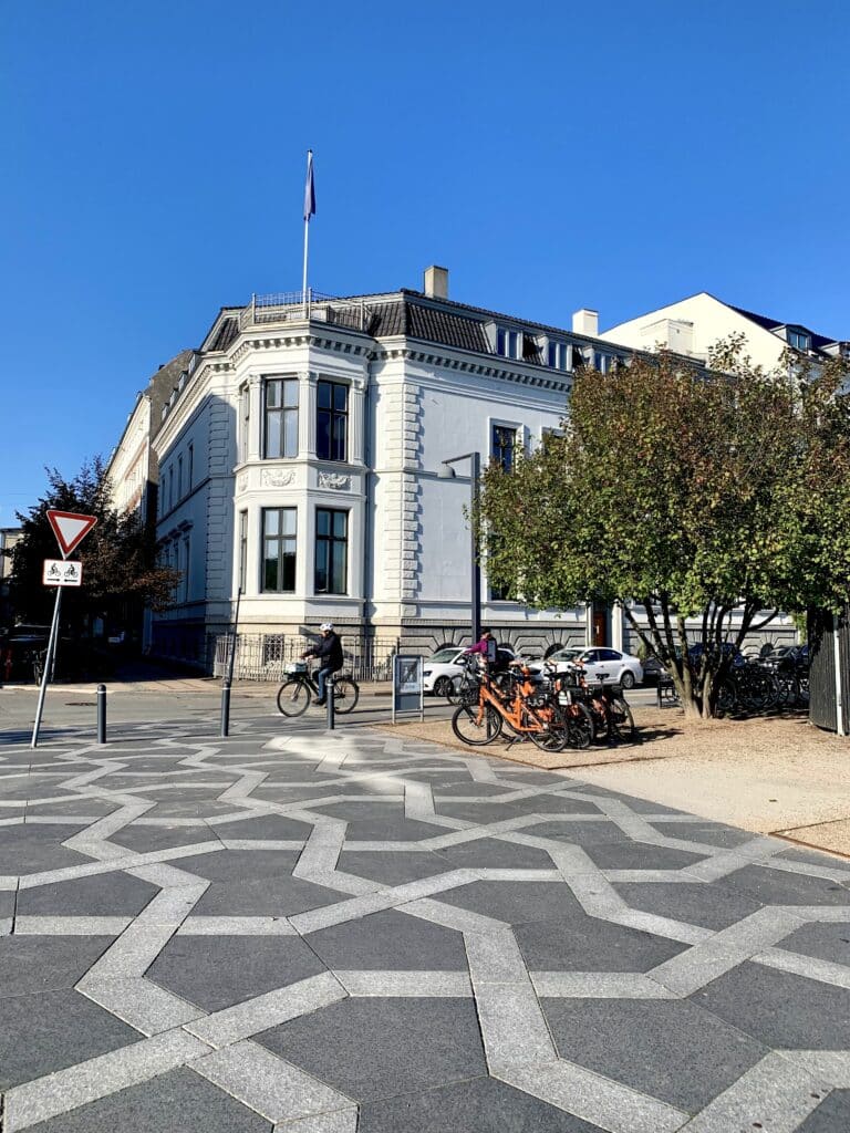Weißes Eckhaus und Fahrräder auf einem Platz mit geometrischem Pflastermuster
