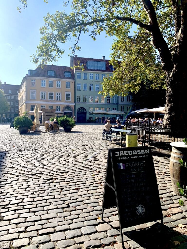 Gepflasterter Platz mit Cafétischen und Häusern in der Sonne