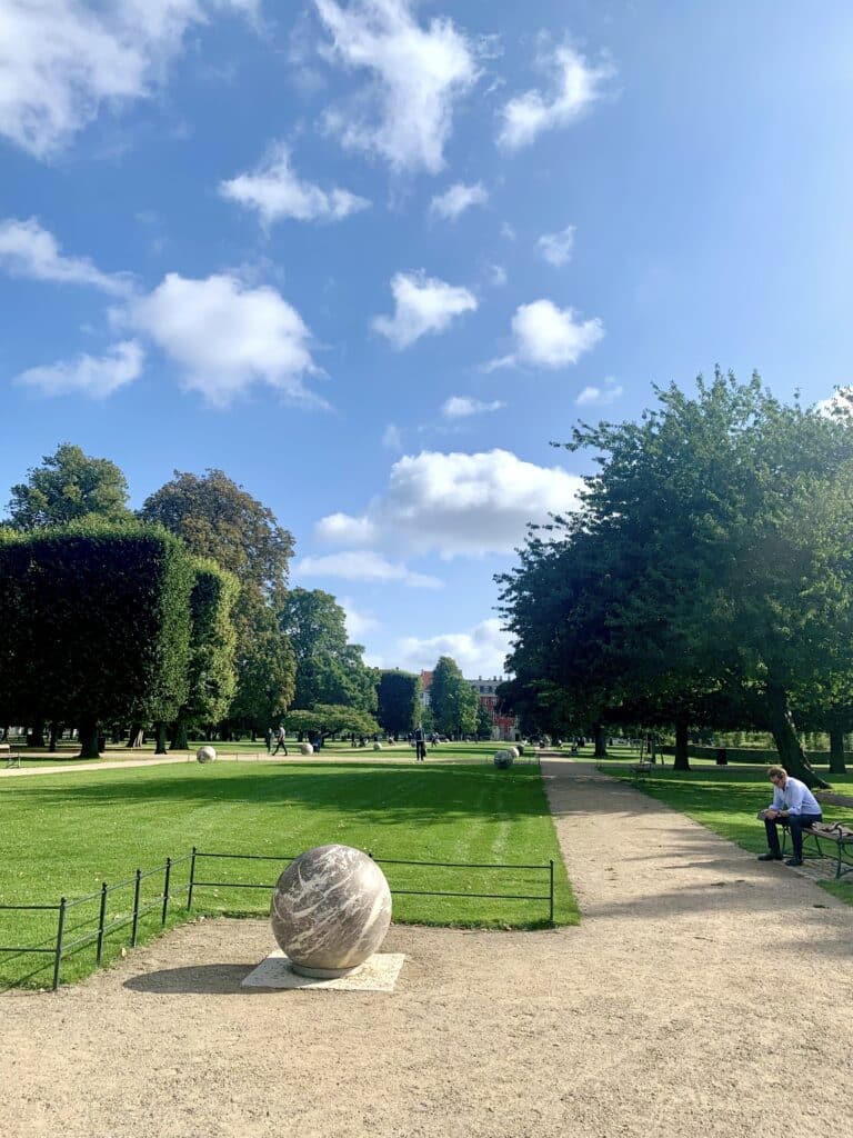 Park mit Weg, geschnittener Hecke und Steinkugel auf dem Rasen