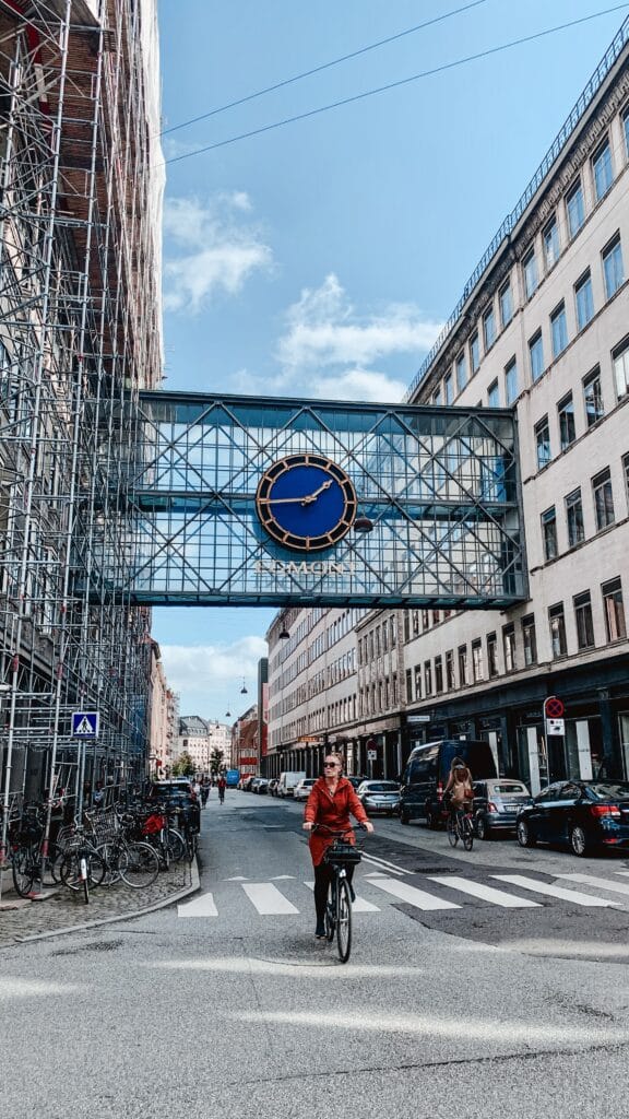 Radfahrer auf der Straße unter einer verglasten Brücke mit großer Uhr