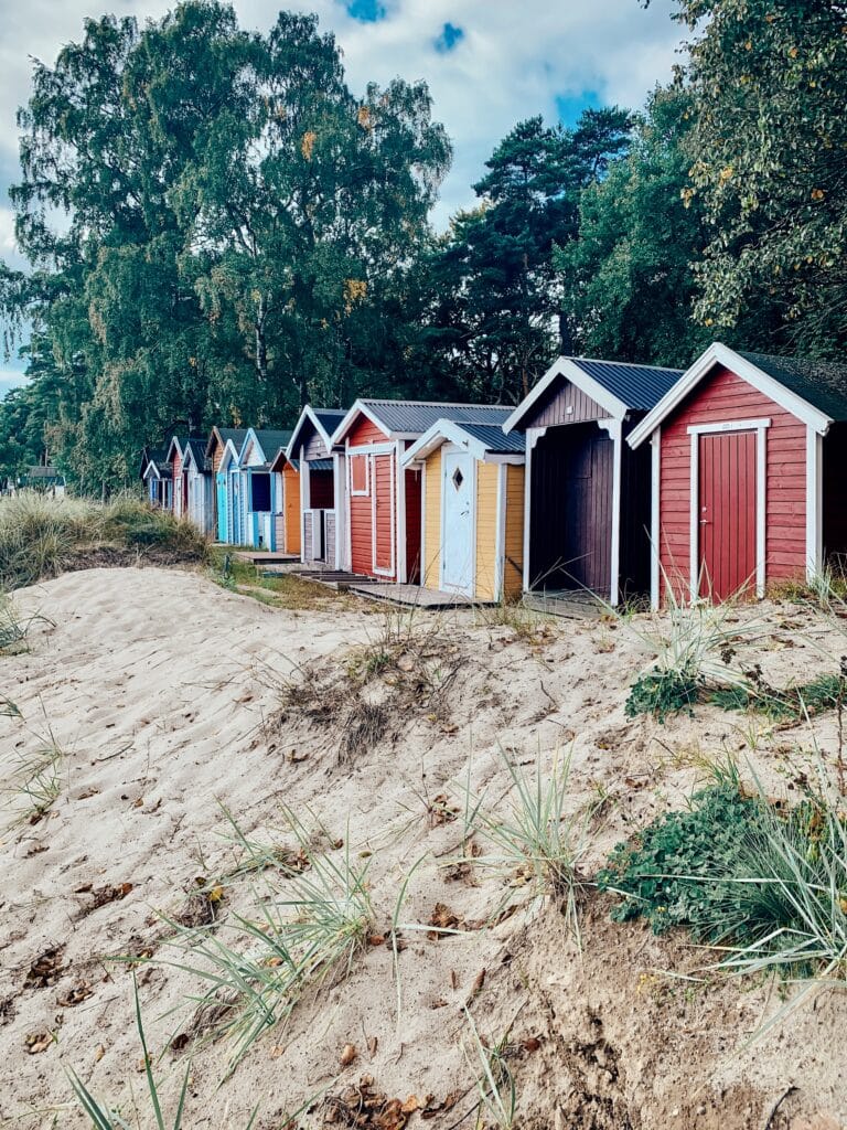 Bunte Strandhäuschen aus Holz auf einer Düne zwischen Bäumen in Ystad