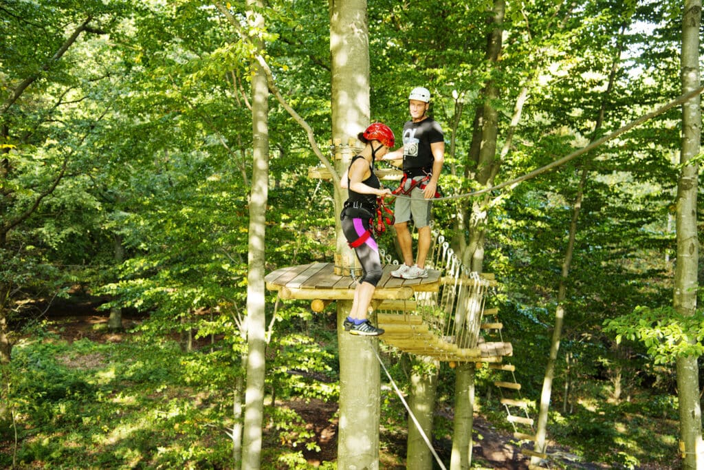 Zwei Personen mit Helm auf einer Holzplattform im Kletterwald