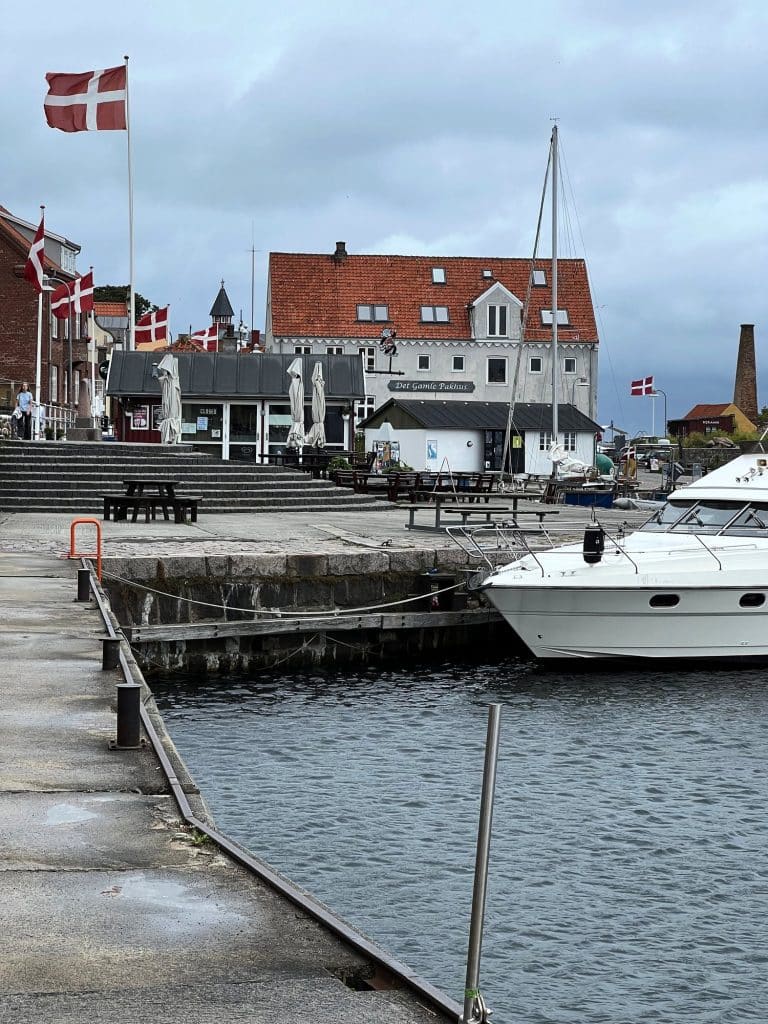 Hafen von Allinge: Kai mit einer Yacht, dänische Flaggen und das Gebäude Det Gamle Pakhus