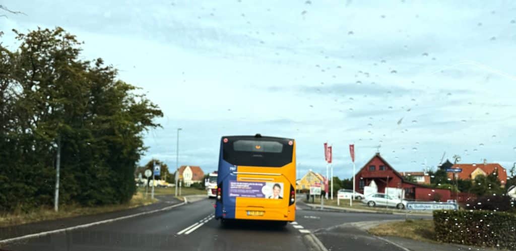 Gelb-blauer BAT-Bus auf der Straße bei der Einfahrt nach Gudhjem, Blick durch die nasse Windschutzscheibe