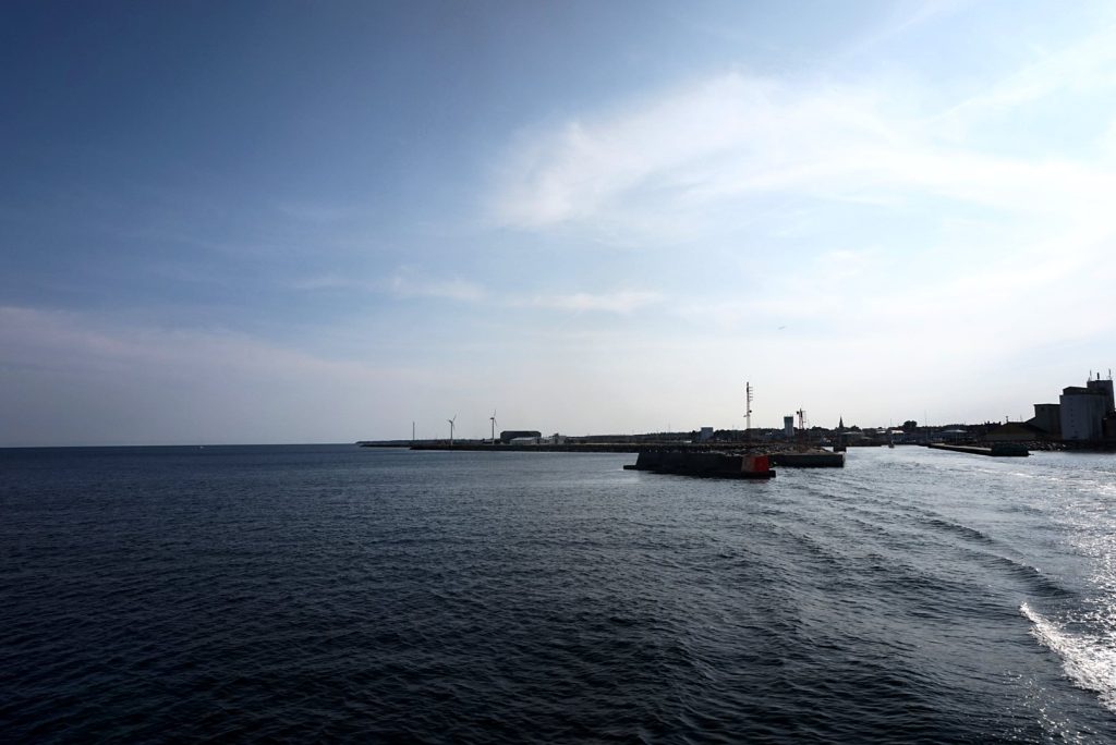Hafeneinfahrt von Nexø vom Meer aus gesehen, Mole, Silos und Windräder, rechts schäumendes Kielwasser