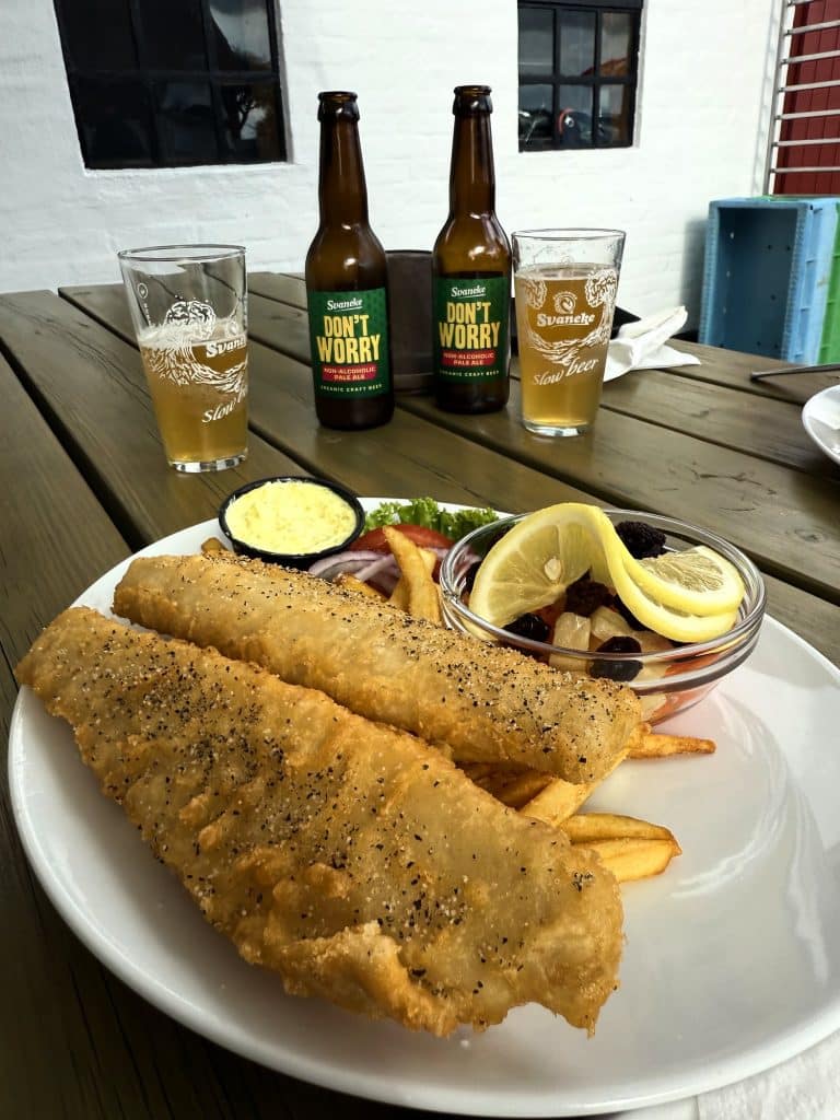 Panierter Fisch mit Pommes und zwei Flaschen Don’t Worry von Svaneke Bryghus auf einem Tisch in der Nexø Gamle Røgeri