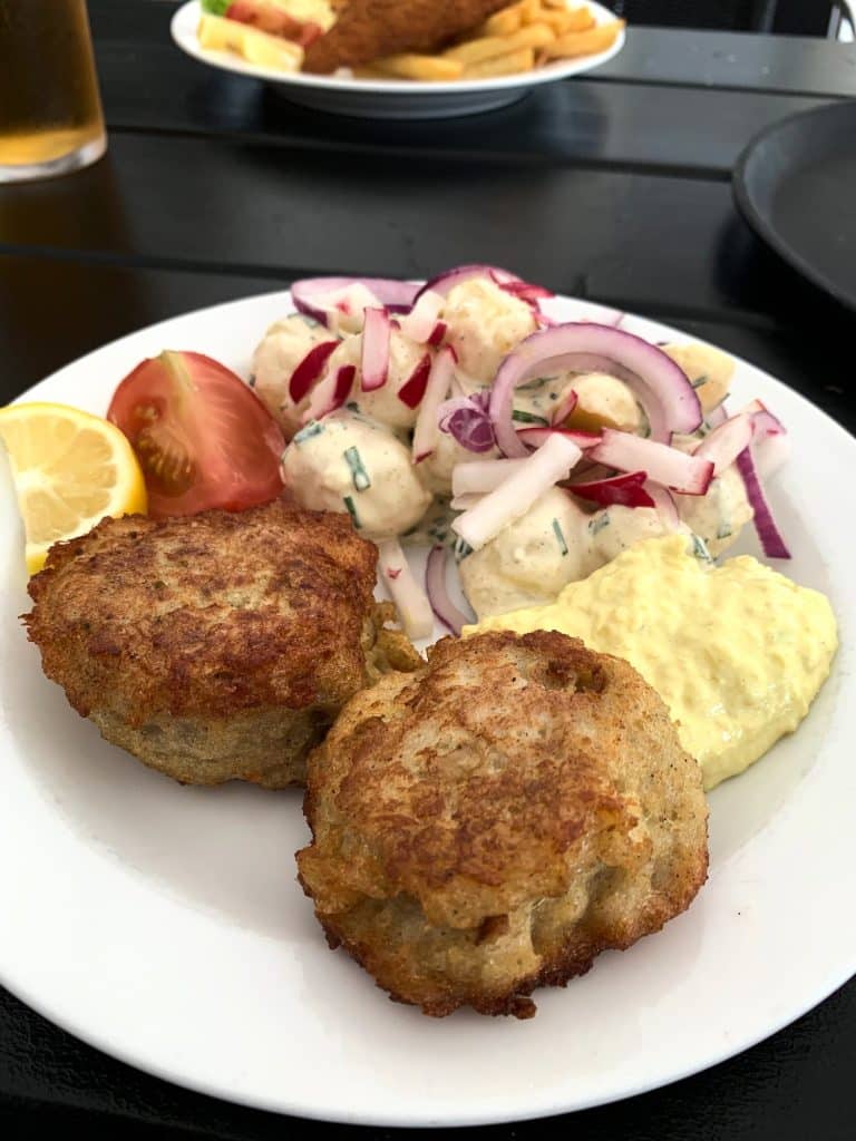 Zwei Fischfrikadellen (fiskefrikadeller) mit Remoulade, Kartoffelsalat, Tomate und Zitrone auf einem Teller