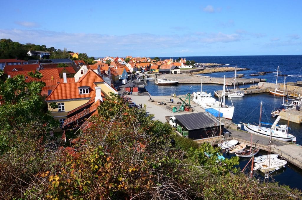 Der Hafen von Gudhjem von oben: Boote am Kai, rote Hausdächer und die Ostsee
