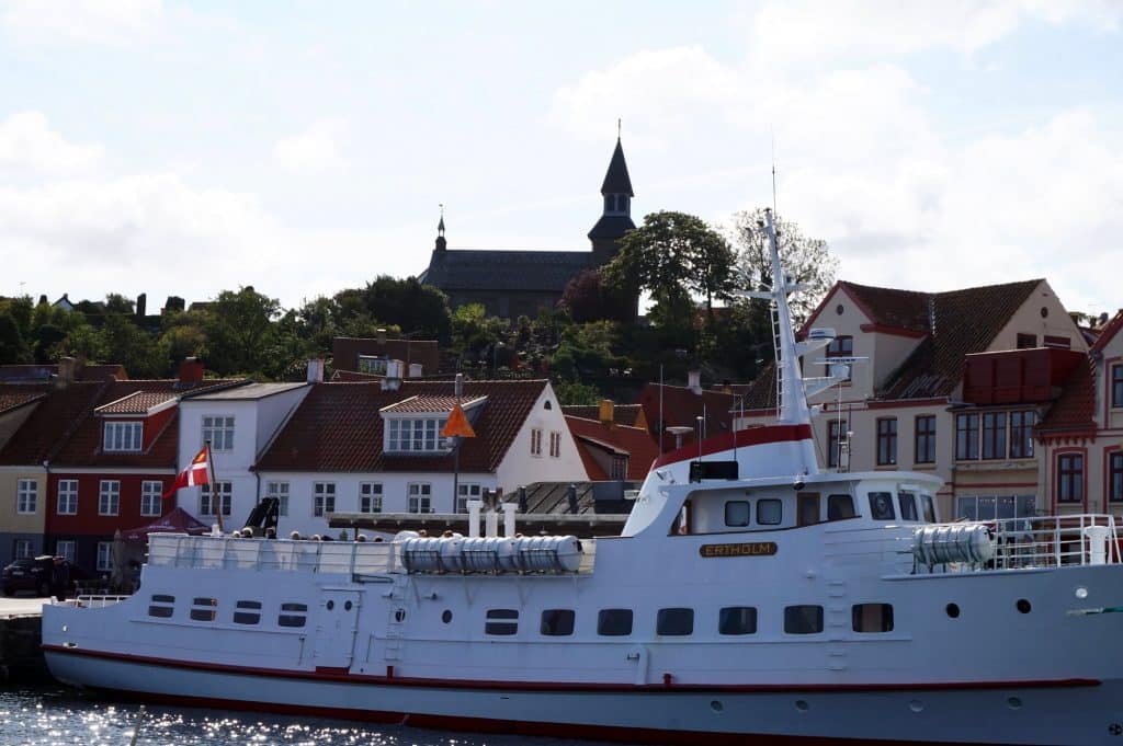 Weißes Schiff nach Christiansø am Kai in Gudhjem, über dem Hafen ein Kirchturm