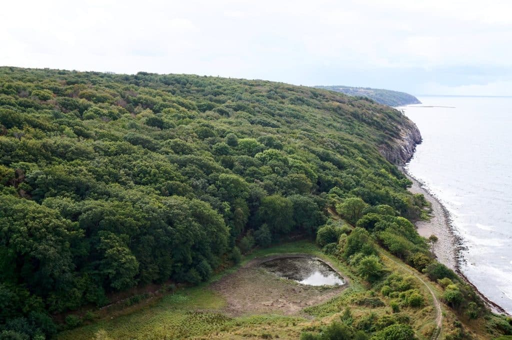Blick von den Mauern von Hammershus auf bewaldete Hänge, einen kleinen Teich und die Küste
