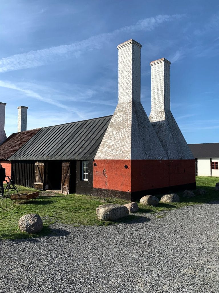 Weiße Schornsteine der Hasle Røgeri mit rotem Sockel, vor dem Gebäude Findlinge auf Kies