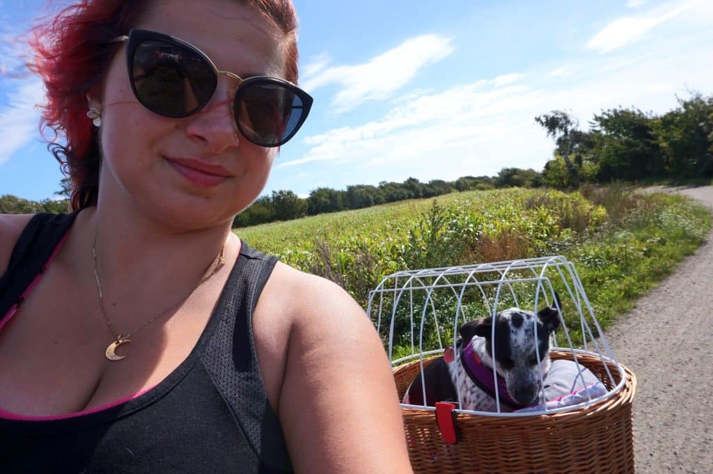 Ewelina mit Hund im Weidenkorb am Fahrrad auf einem Weg zwischen Feldern bei Hasle