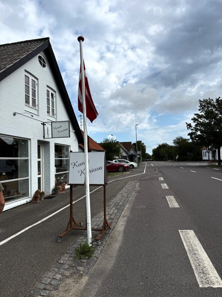 Weißes Haus mit dem Laden Kunst Kuriosa in Østermarie, Schild und dänische Flagge an der Straße