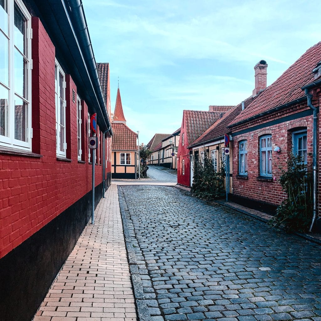 Gepflasterte Gasse mit roten Backsteinhäusern in Rønne, im Hintergrund ein spitzes Türmchen