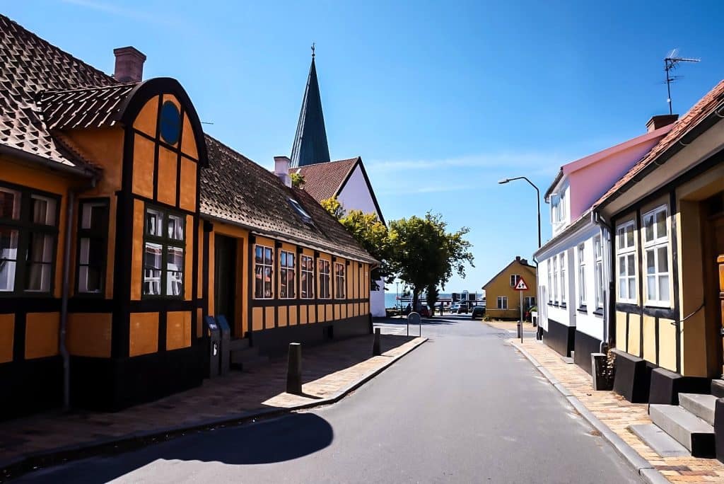 Straße in Rønne mit gelben Fachwerkhäusern, im Hintergrund ein Kirchturm