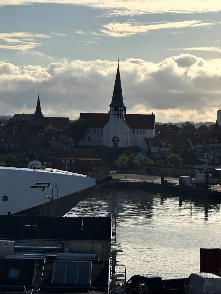 Rønne im Morgengrauen vom Fährdeck aus: die Nikolaikirche über dem Hafen und der Bug der Fähre am Kai