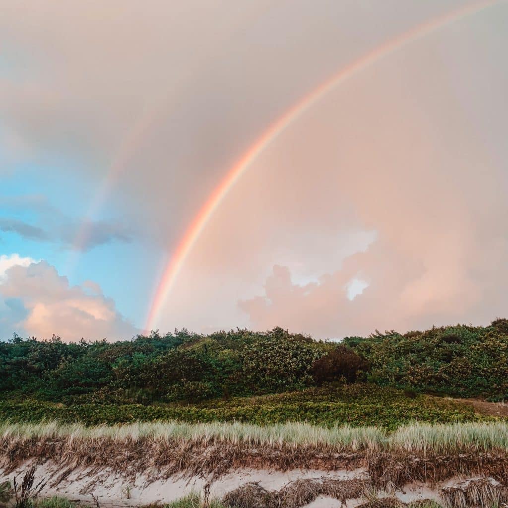 Doppelter Regenbogen über bewachsenen Dünen am Strand von Rønne, rosa Abendhimmel