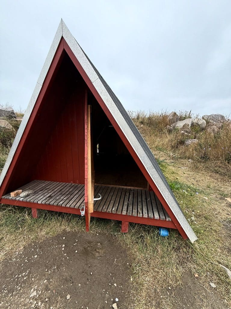 Roter Holz-Shelter in A-Form mit Bretterboden, vorne offen, zwischen trockenen Gräsern