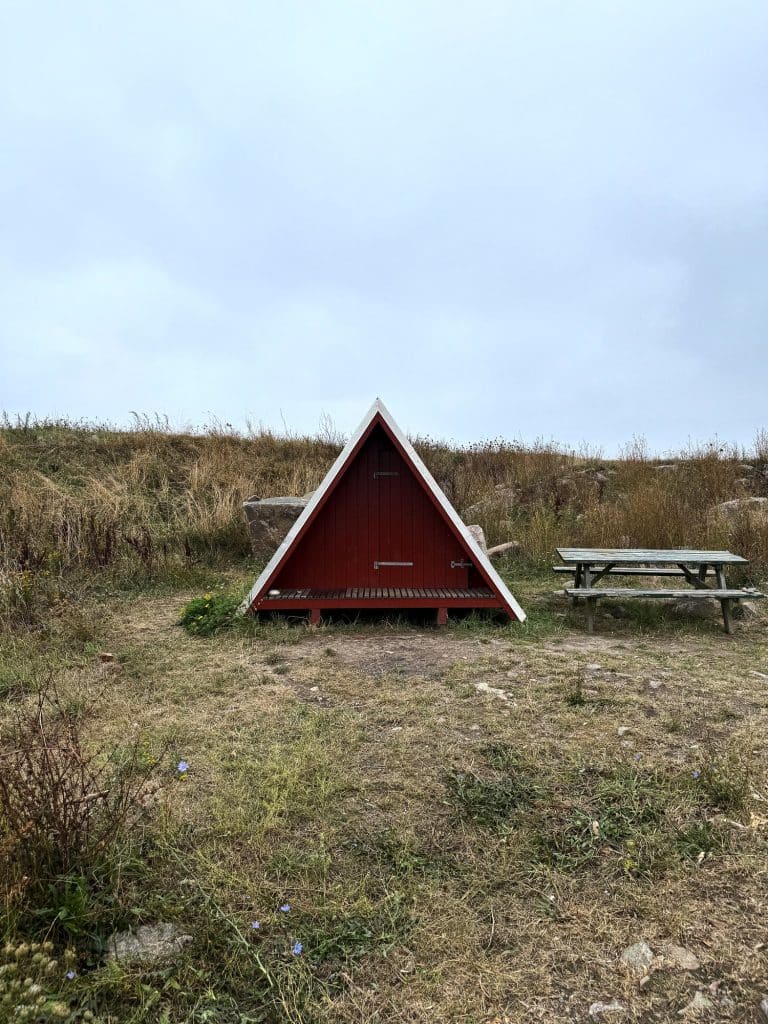 Roter Shelter in A-Form und ein Picknicktisch aus Holz auf einer Wiese