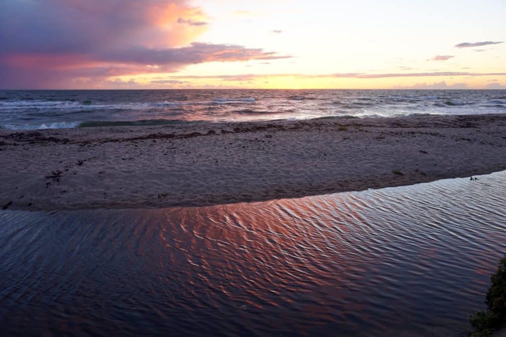 Sonnenuntergang über dem Meer, im Vordergrund Rippeln im Sand der flachen Bachmündung