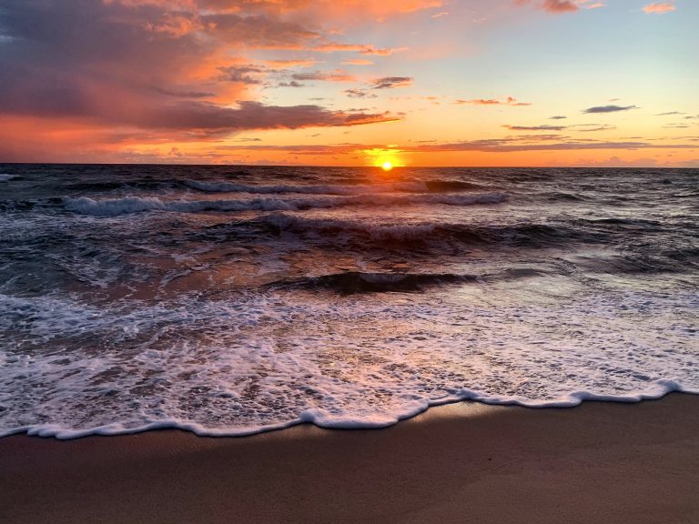 Untergehende Sonne über der Ostsee, schäumende Welle am Sandstrand