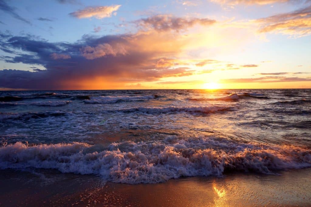 Untergehende Sonne über der aufgewühlten Ostsee, Wellen brechen am sandigen Ufer