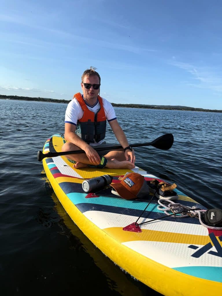 Mann mit Schwimmweste sitzt mit Paddel auf einem gelben SUP-Board auf ruhigem Meer
