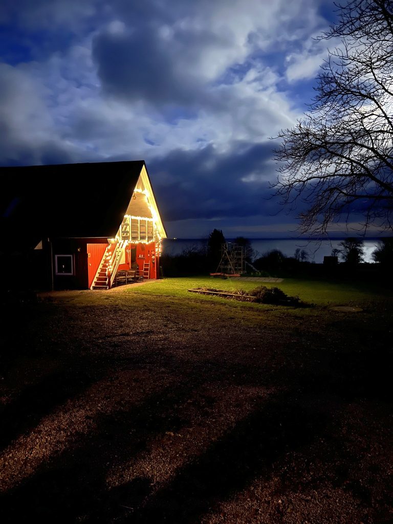 Ferienwohnungen bei Gudhjem mit Weihnachtsbeleuchtung am Abend, dahinter die Ostsee
