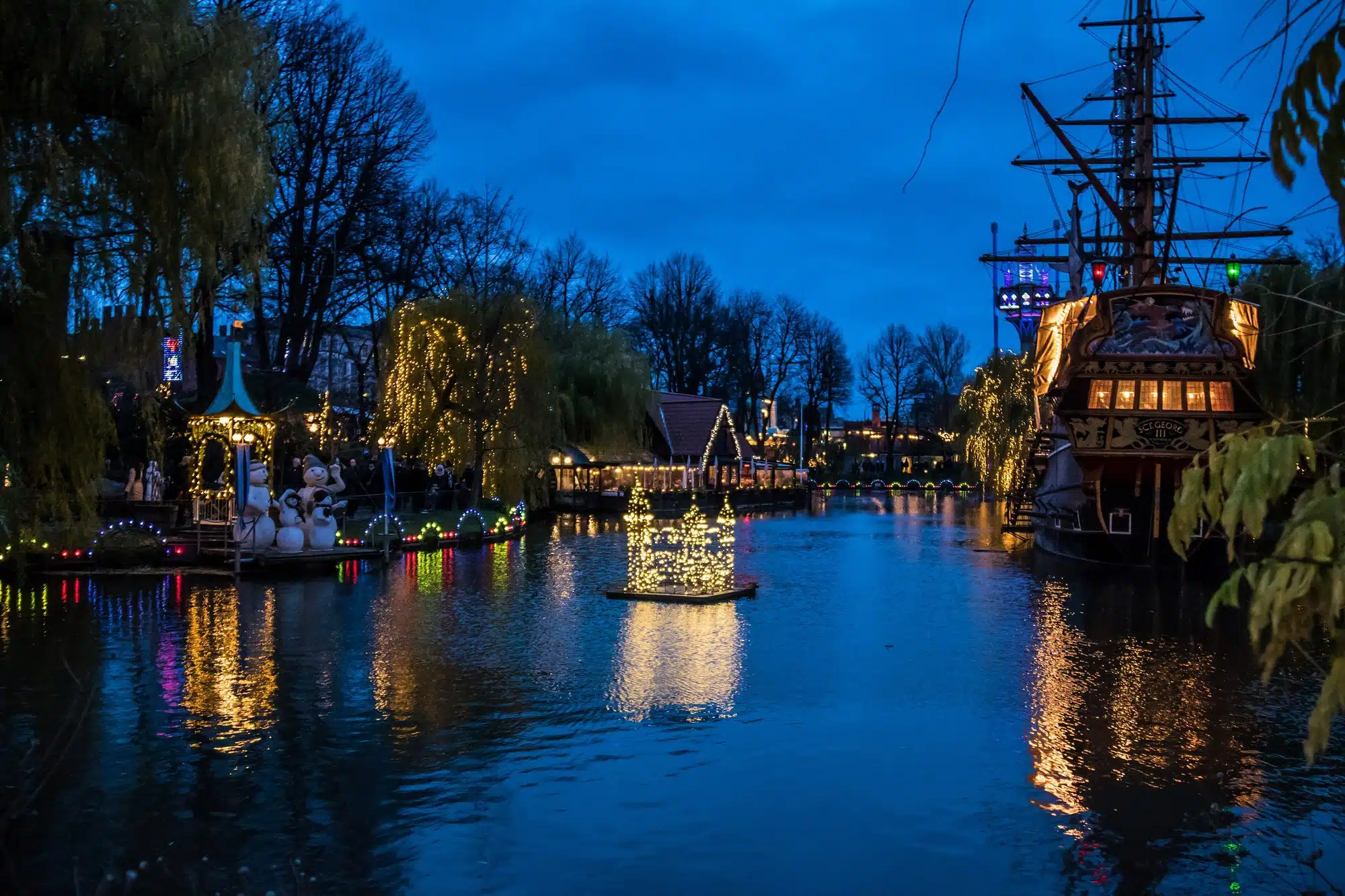 Tivoli-Gärten in Kopenhagen bei Nacht in weihnachtlicher Beleuchtung, Teich und Schiff